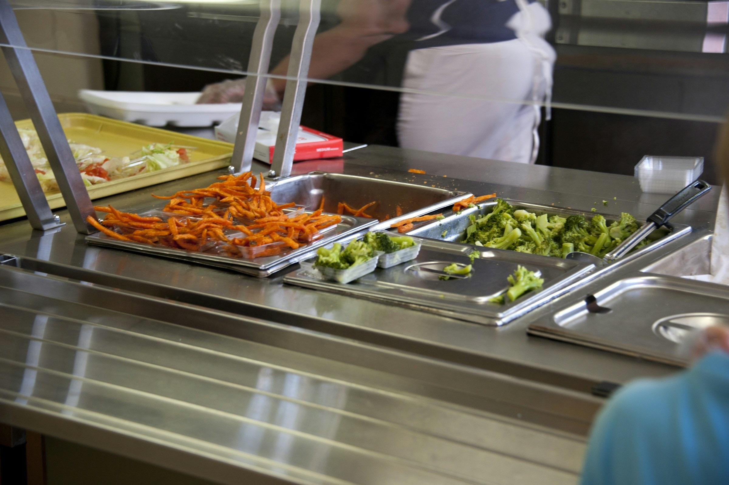 Ligne de self d’une cantine scolaire : bacs gastronormes de carottes et de brocolis sous la vitre de protection.